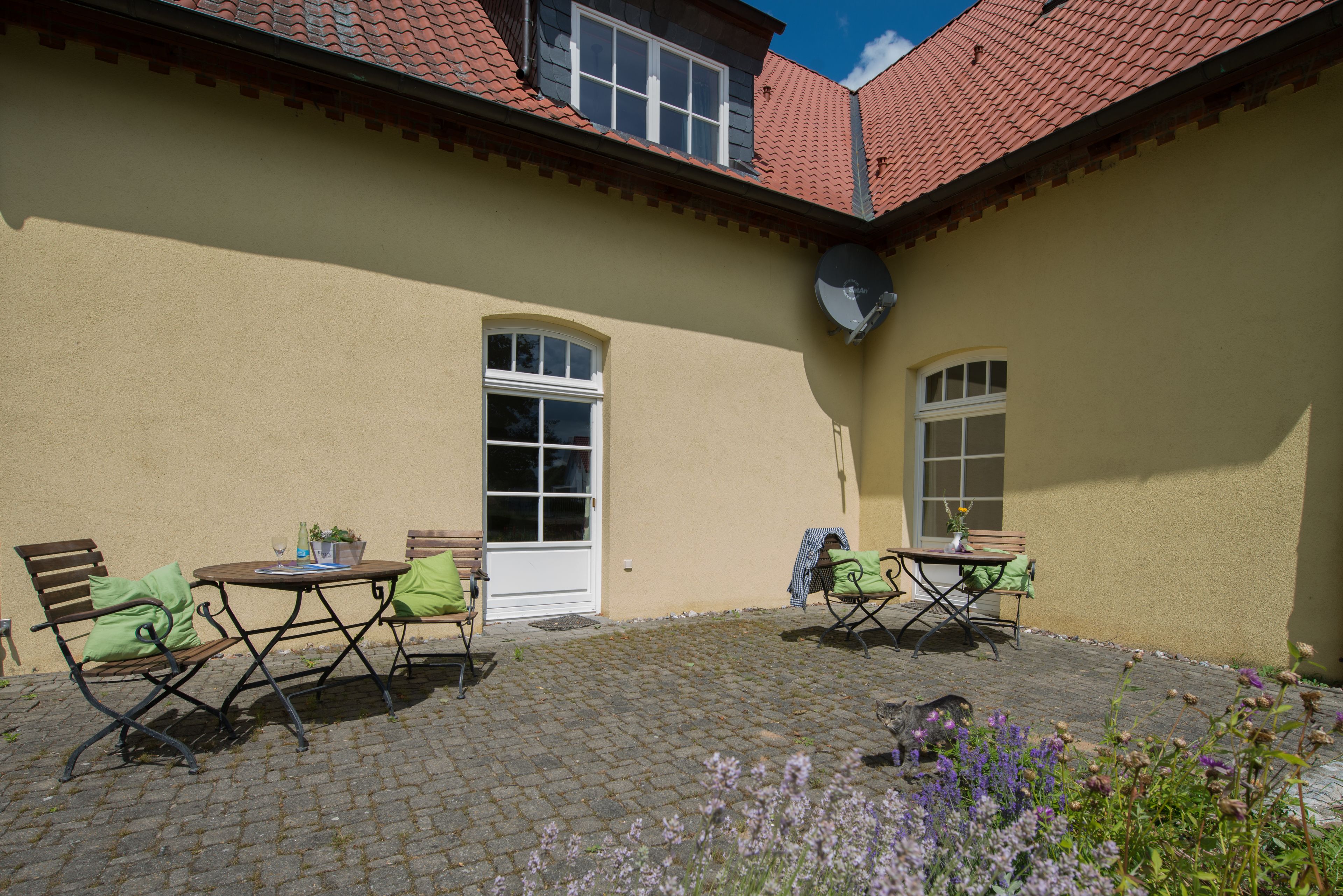 Ein Innenhof mit Kopfsteinpflaster, zwei Tische mit Stühlen und einer Tür.