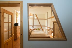 A bedroom with a sloped ceiling, wooden beams, a bed with pillows, a nightstand, and a hanging light fixture. - Ostsee-Landhaus (Bastorf)