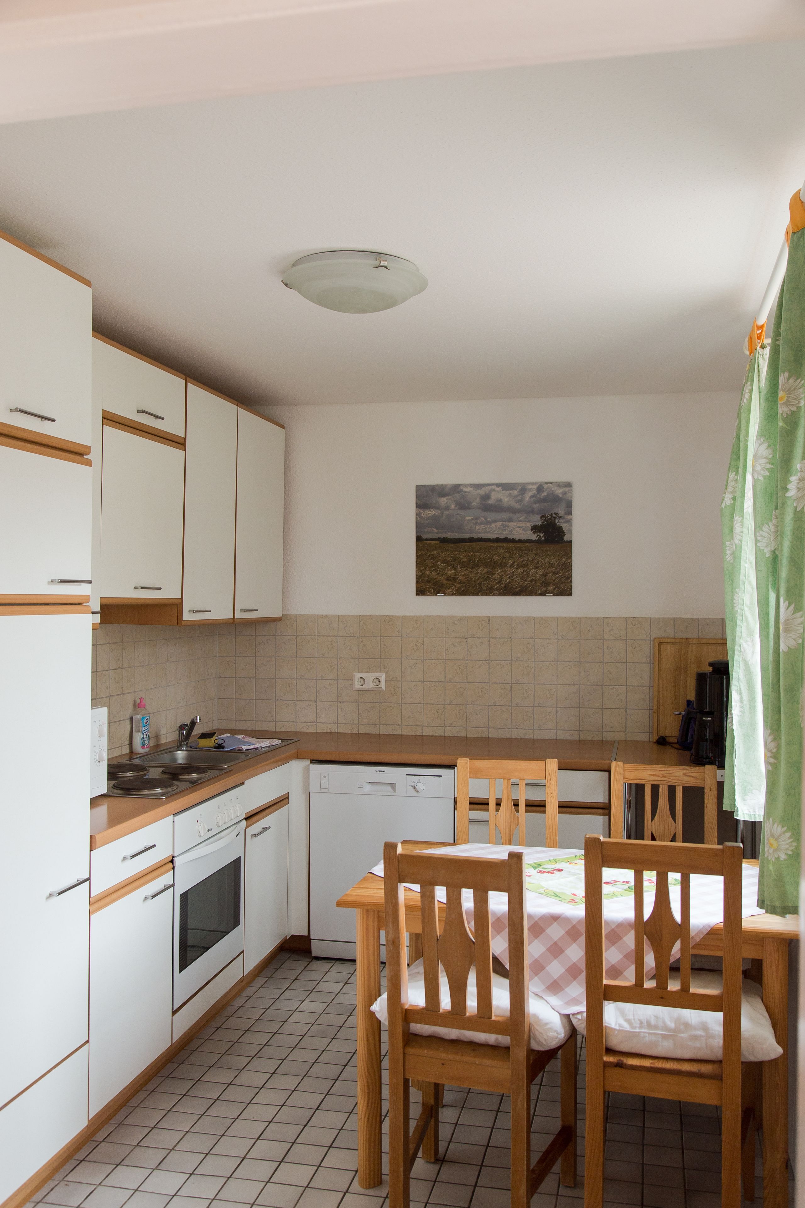 A kitchen with white cabinets, a wooden countertop, a dining table with chairs, and a ceiling light.