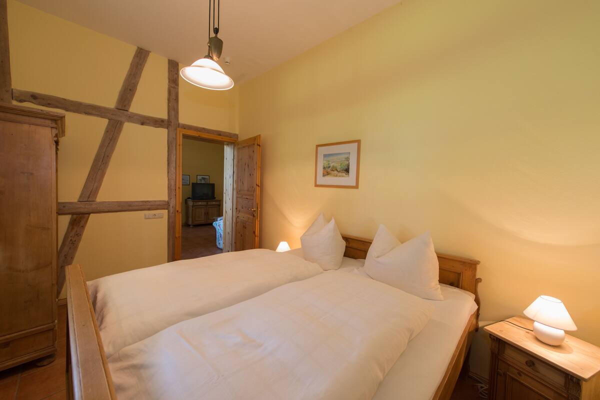 Une chambre avec deux lits, des têtes de lit en bois, une lampe de chevet et un tableau encadré au mur.