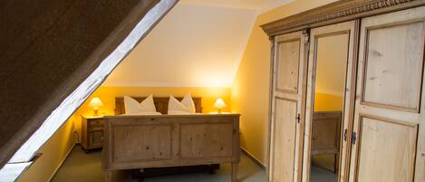 A bedroom with a sloped ceiling, a wooden bed with pillows, a nightstand with a lamp, and a wooden wardrobe.