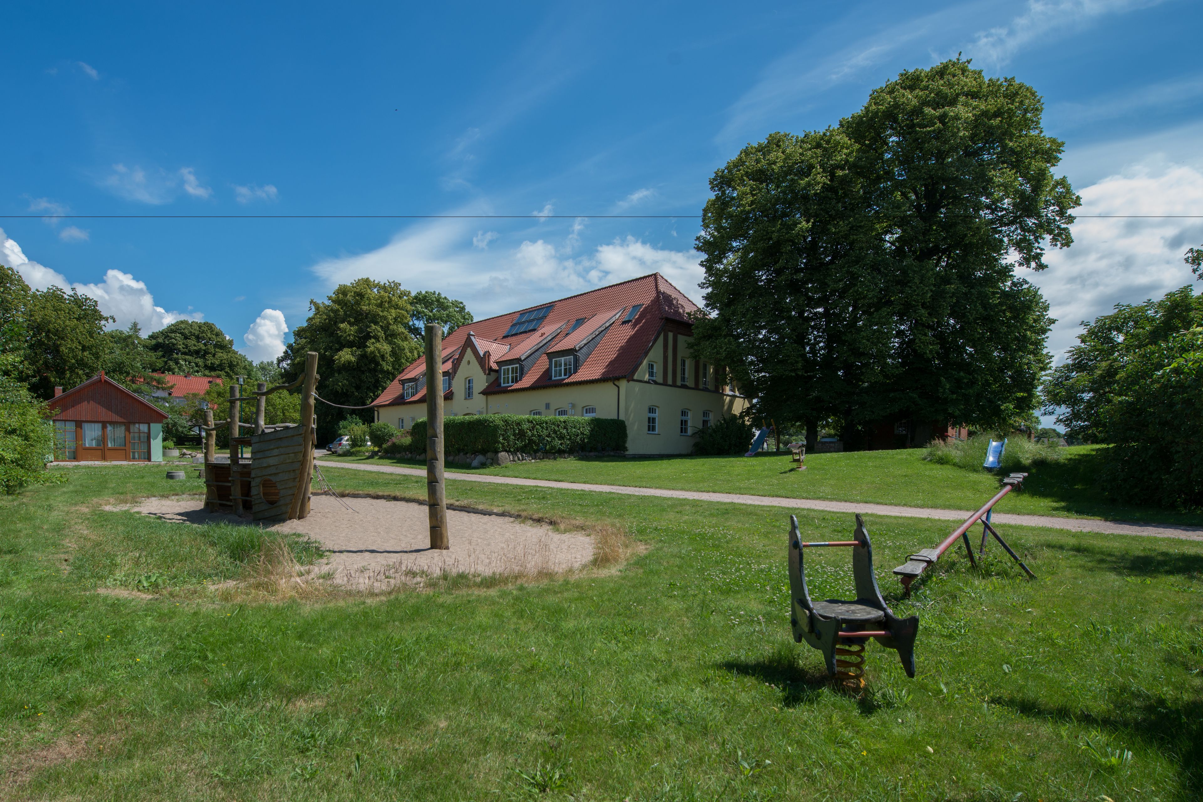 Ett stort hus med ett rött tak, omgivet av en gräsyta med en gunga och en träkonstruktion.