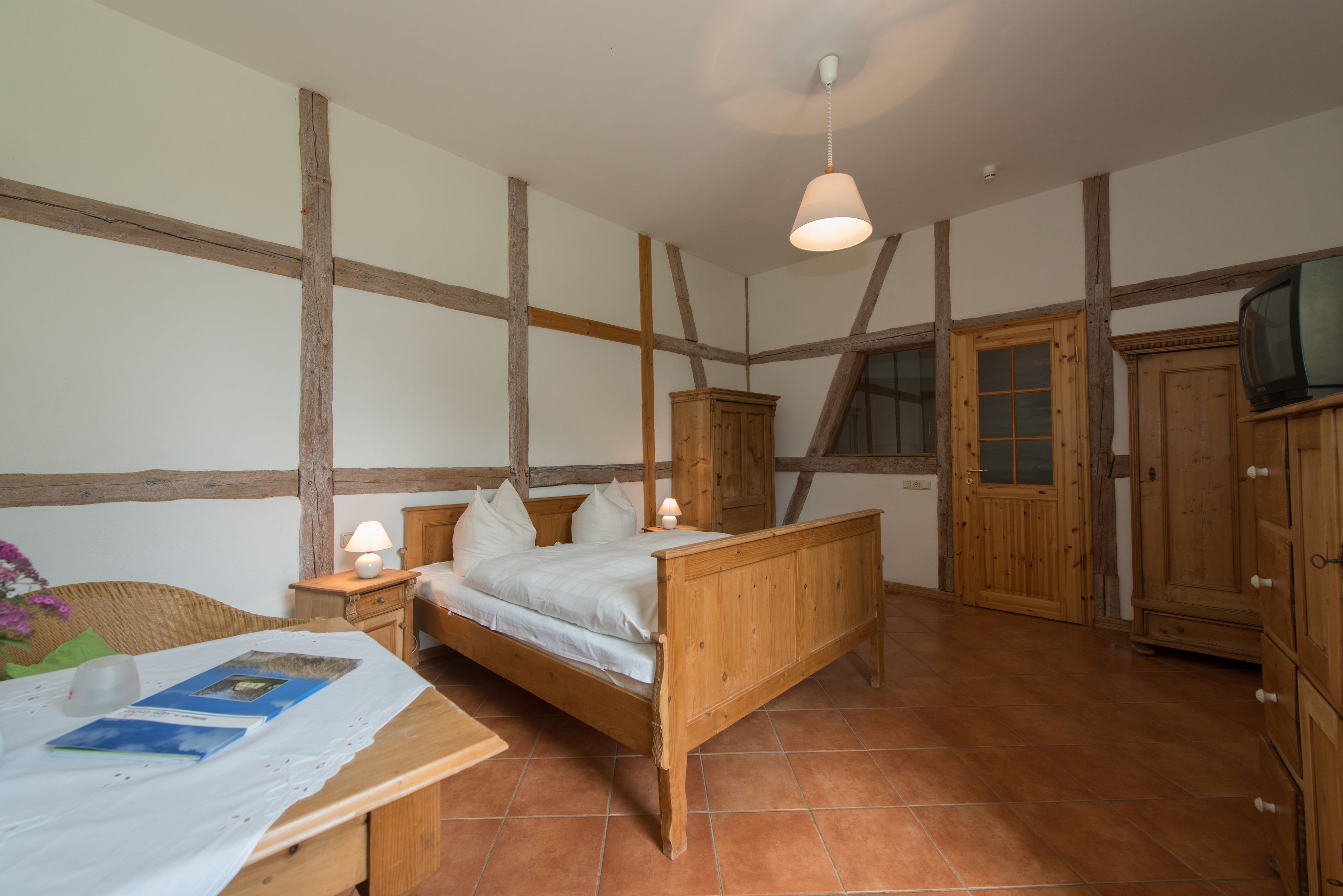 A bedroom with a wooden bed, a nightstand, a lamp, a wooden wardrobe, and a television.