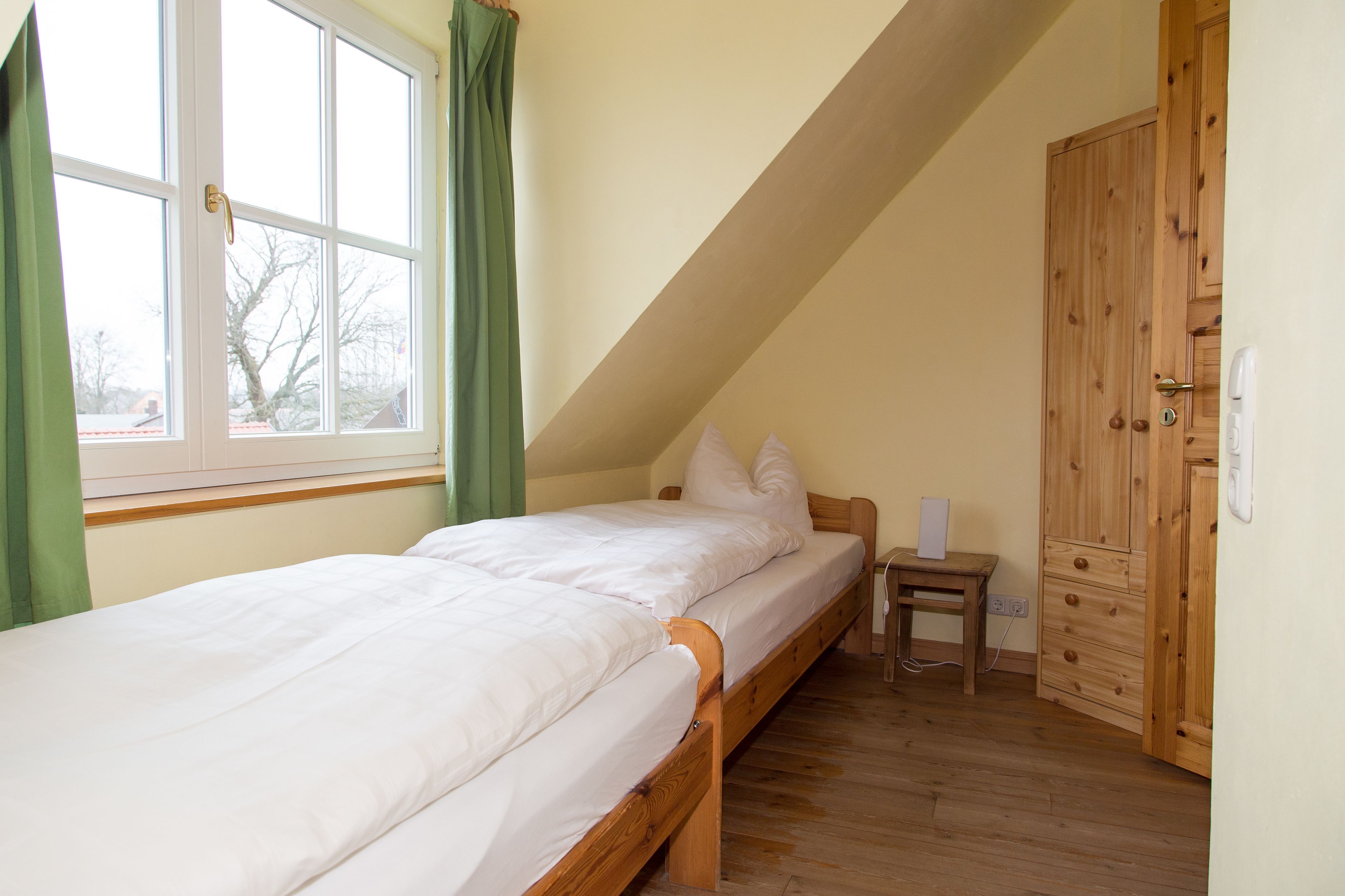 A single bed with white bedding in a room with a sloped ceiling and wooden flooring.