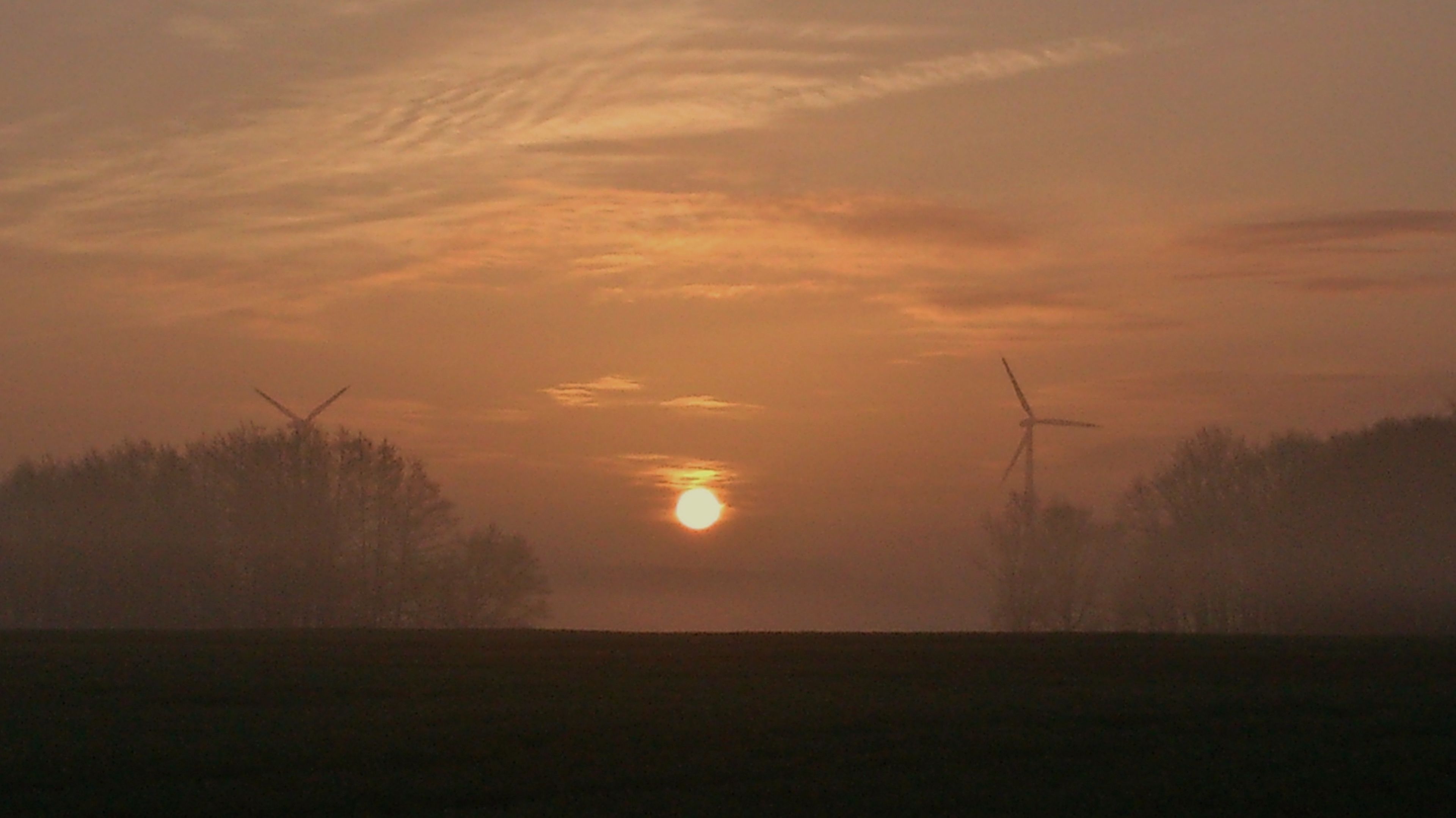 A sunset over a field with wind turbines.