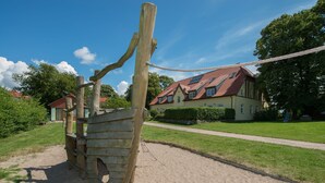 A wooden play structure in a sandy area with a house in the background. - Ostsee-Landhaus (Bastorf)