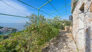 Un chemin de pierre mène à un bâtiment d’où l’on peut admirer une ville côtière et la mer.