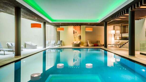 A modern indoor swimming pool with lounge chairs and a staircase. - Foerstlerhof (Postal)