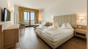 A hotel room with a bed, a desk, a chair, a TV, and a window with curtains. - Foerstlerhof (Postal)