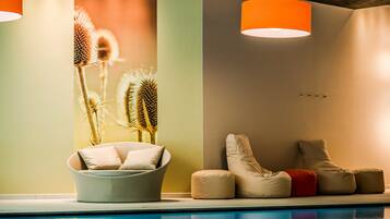 Un espace aménagé au bord de la piscine, comprenant une chaise longue, un pouf et des plantes décoratives.