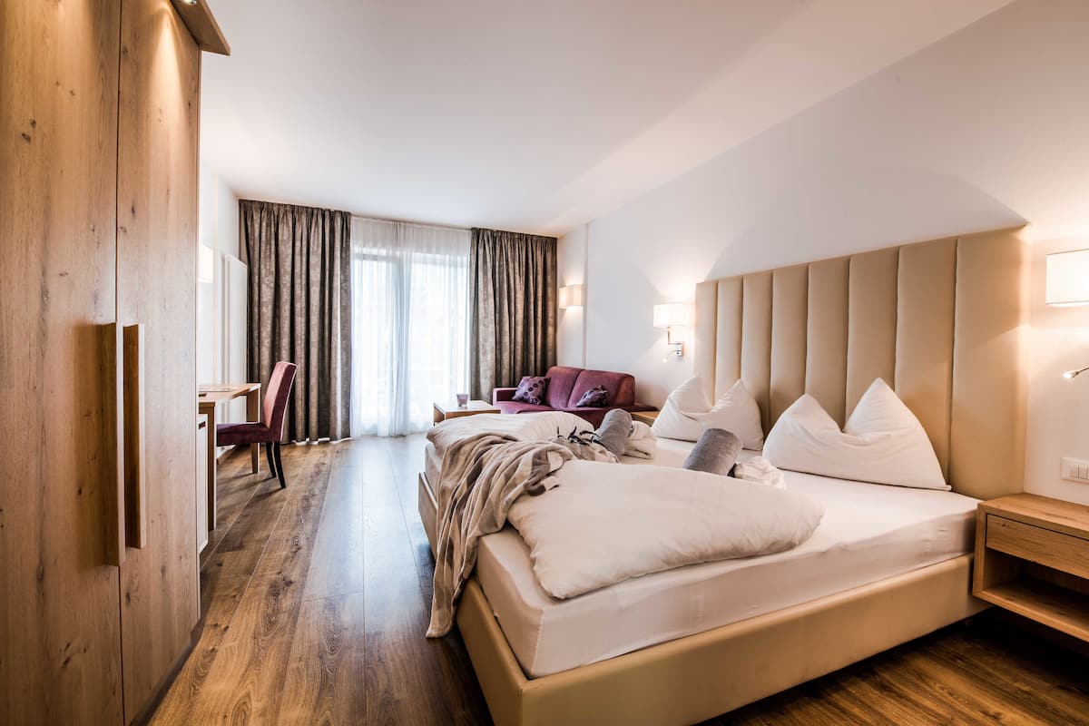 A hotel room with a large bed, a desk, a chair, a sofa, and a wardrobe.
