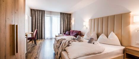 A hotel room with a large bed, a desk, a chair, a sofa, and a wardrobe.