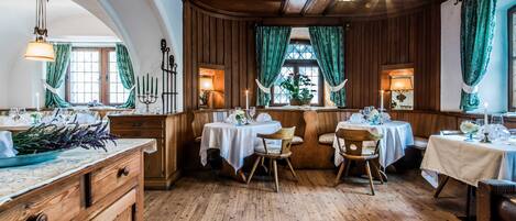 A dining area with wooden paneling, multiple tables set for dining, and green curtains.