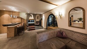 A modern interior with a kitchen area, a seating area with a patterned sofa, and a large mirror on the wall. - Foerstlerhof (Postal)