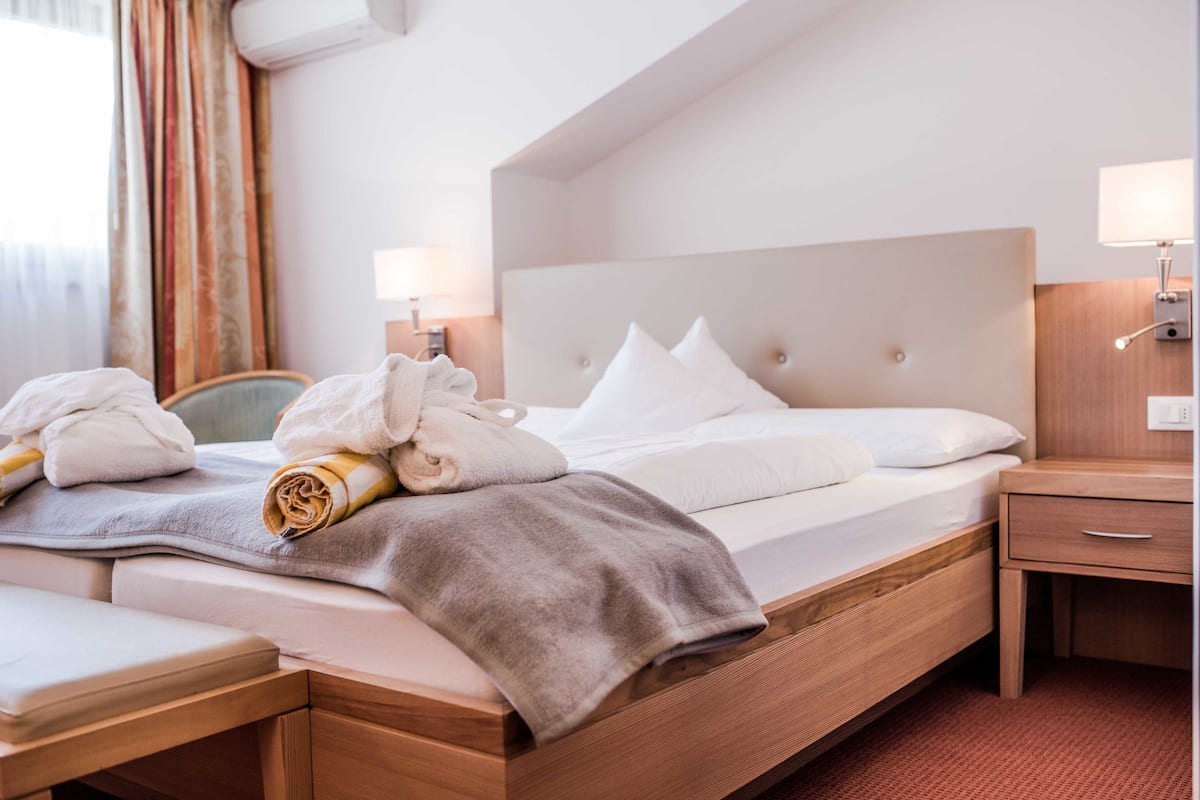 A hotel room with a bed, bedside table, lamp, and a window with curtains.