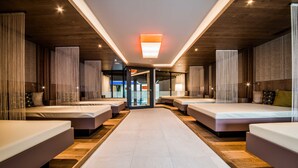 A hotel lobby with a central open space, multiple beds arranged in rows, and a modern ceiling design. - Foerstlerhof (Postal)