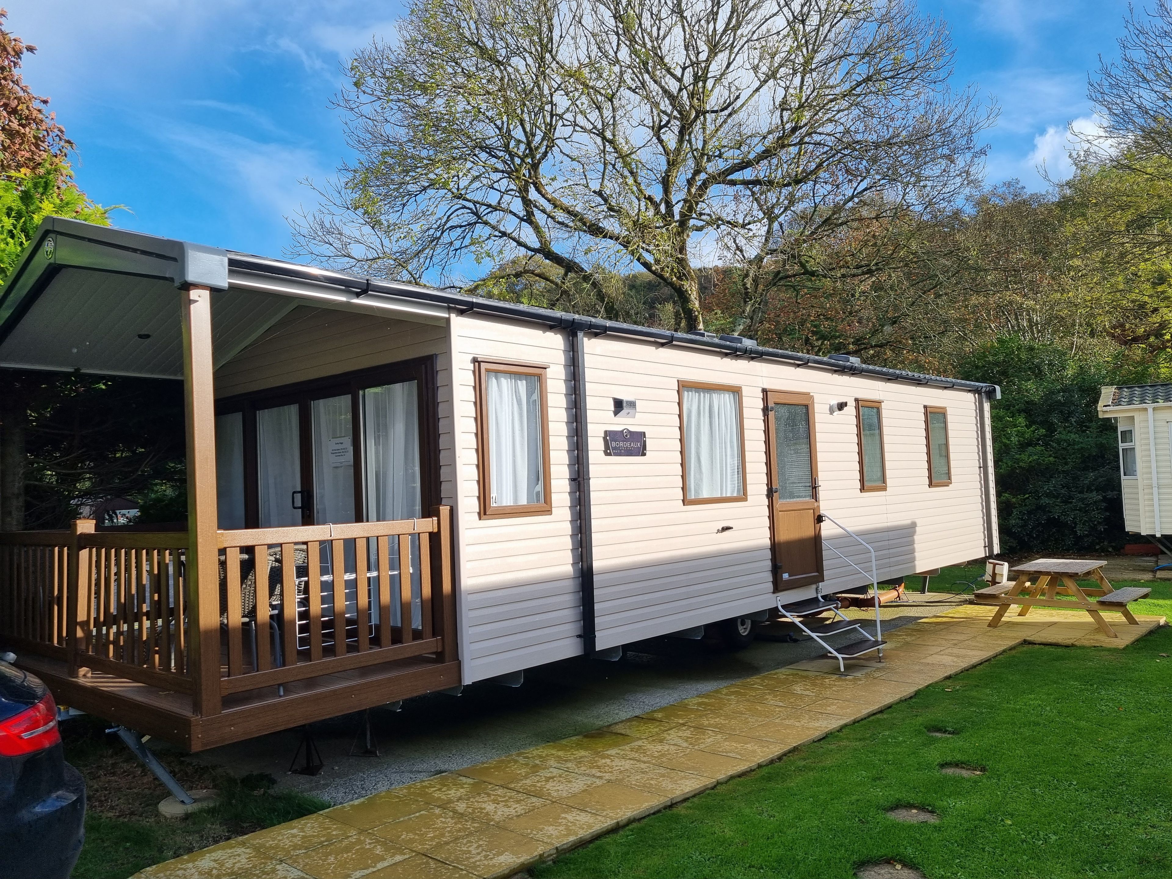 A mobile home with a covered porch, a small deck, and a paved driveway.