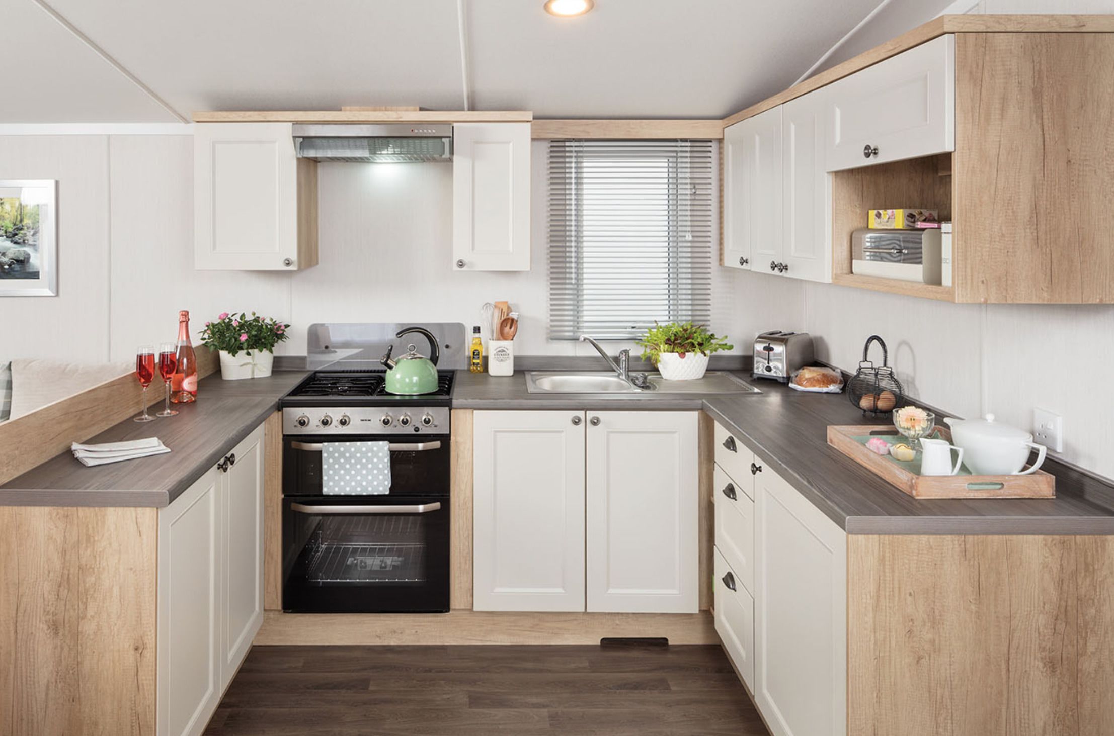 A modern kitchen with white cabinetry, a gas stove, an oven, a sink, and a window with blinds.