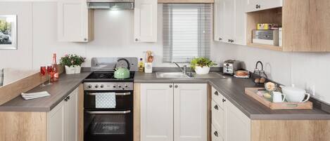 A modern kitchen with white cabinetry, a gas stove, an oven, a sink, and a window with blinds.