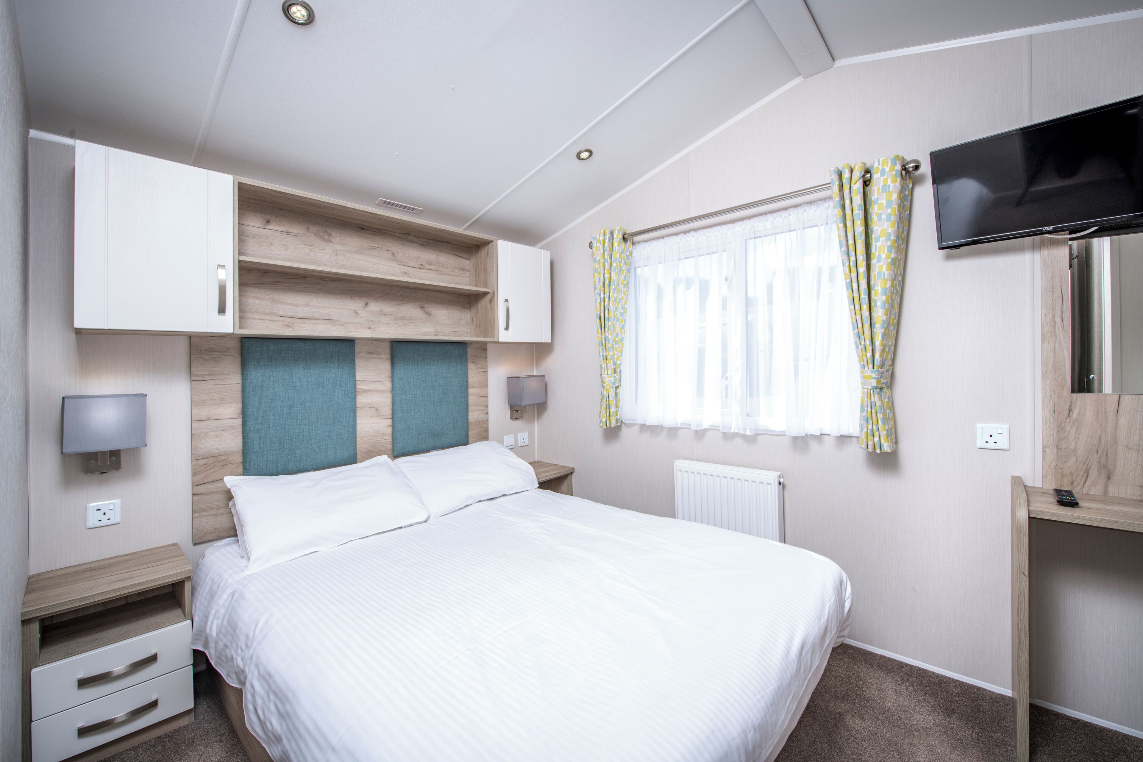 Une chambre d’hôtel avec un lit, une télévision, un bureau et une fenêtre avec des rideaux.