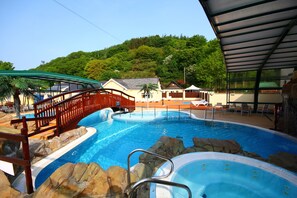 A swimming pool with a wooden bridge, lounge chairs, and a hot tub. - Cardigan Bay Holiday Park (Cardigan)