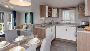 A modern RV kitchen with wooden cabinets, a dining area with a table set for four, and a large window providing natural light. - Cardigan Bay Holiday Park (Cardigan)