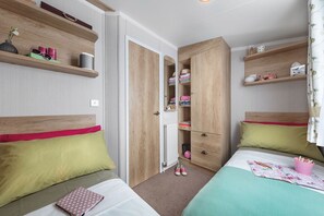 A bedroom with two beds, wooden wardrobes, and shelves with personal items. - Cardigan Bay Holiday Park (Cardigan)