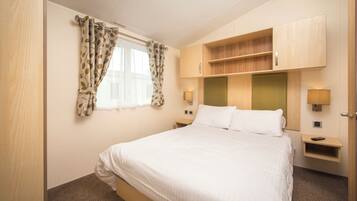 A hotel room with a bed, a window with curtains, a nightstand with a lamp, and built-in shelving.