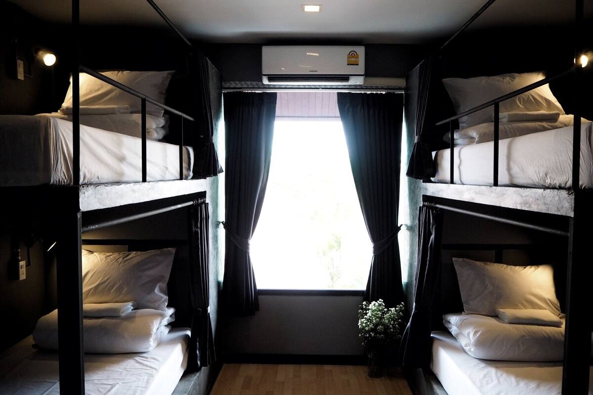 Habitación pequeña con literas, ventana con cortinas y aire acondicionado.