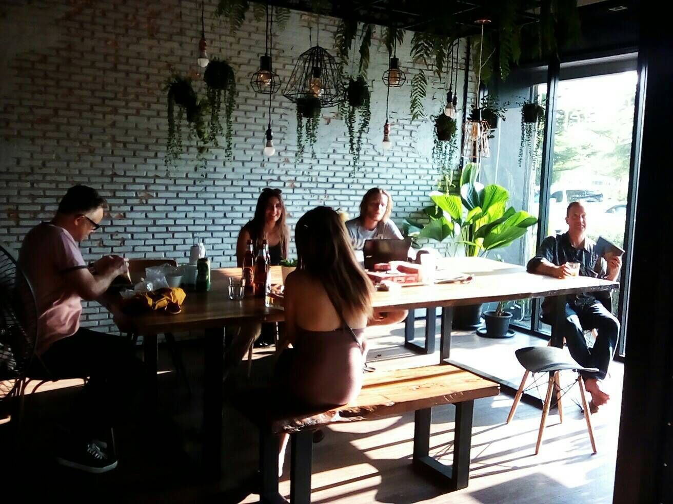 Un comedor con paredes de ladrillo, plantas colgantes y ventanas amplias.