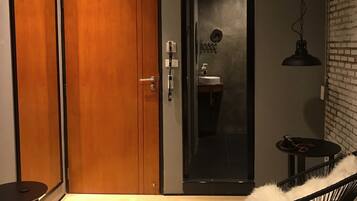 Un dormitorio moderno con una cama grande, un armario de madera, un baño con espejo y una pequeña mesa redonda con una silla.