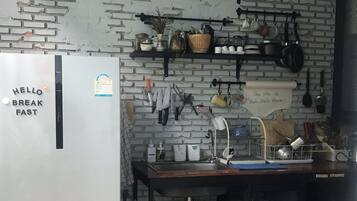 A compact kitchen with a white refrigerator, a sink, and various utensils and dishes on shelves.