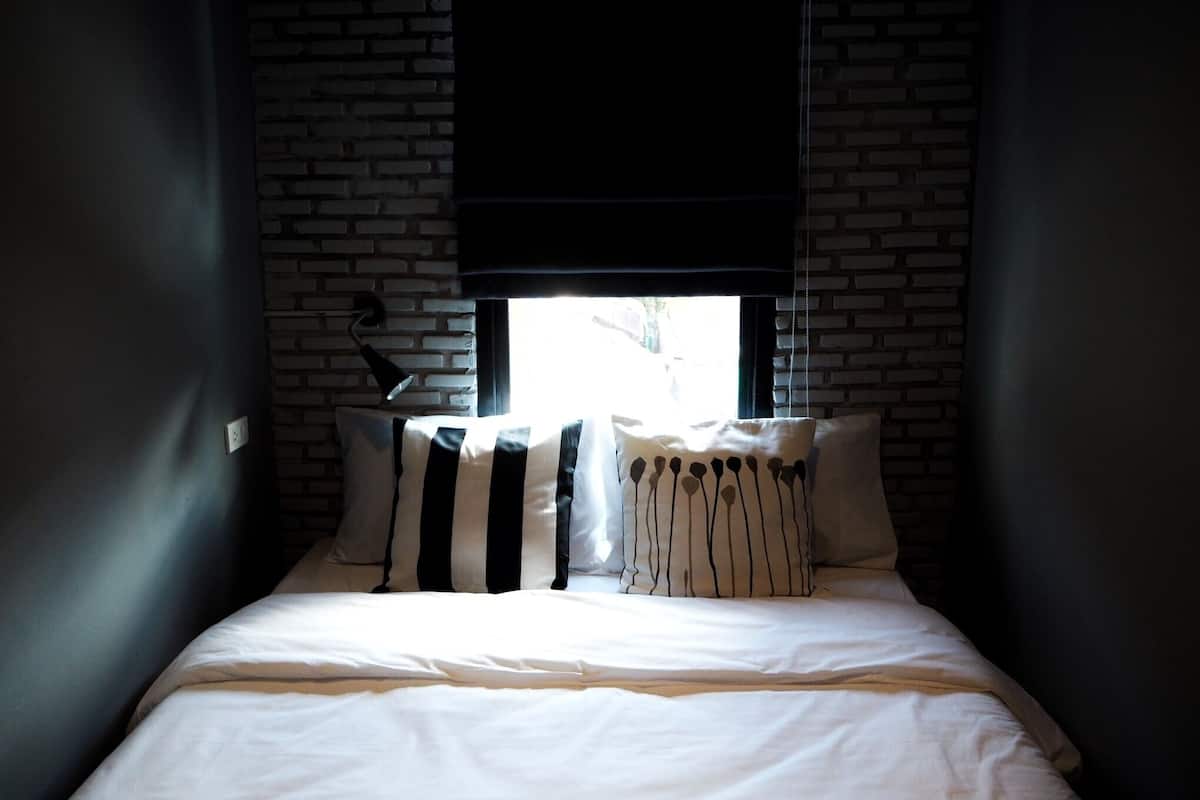 Una cama con ropa de cama blanca, almohadas a rayas negras y blancas y un cabecero negro.