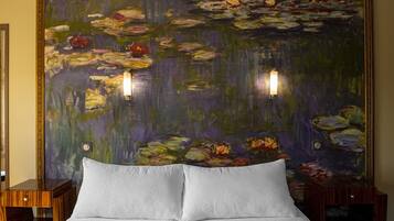 A hotel room with a large floral painting on the wall, a bed with white linens, and two bedside tables with lamps.