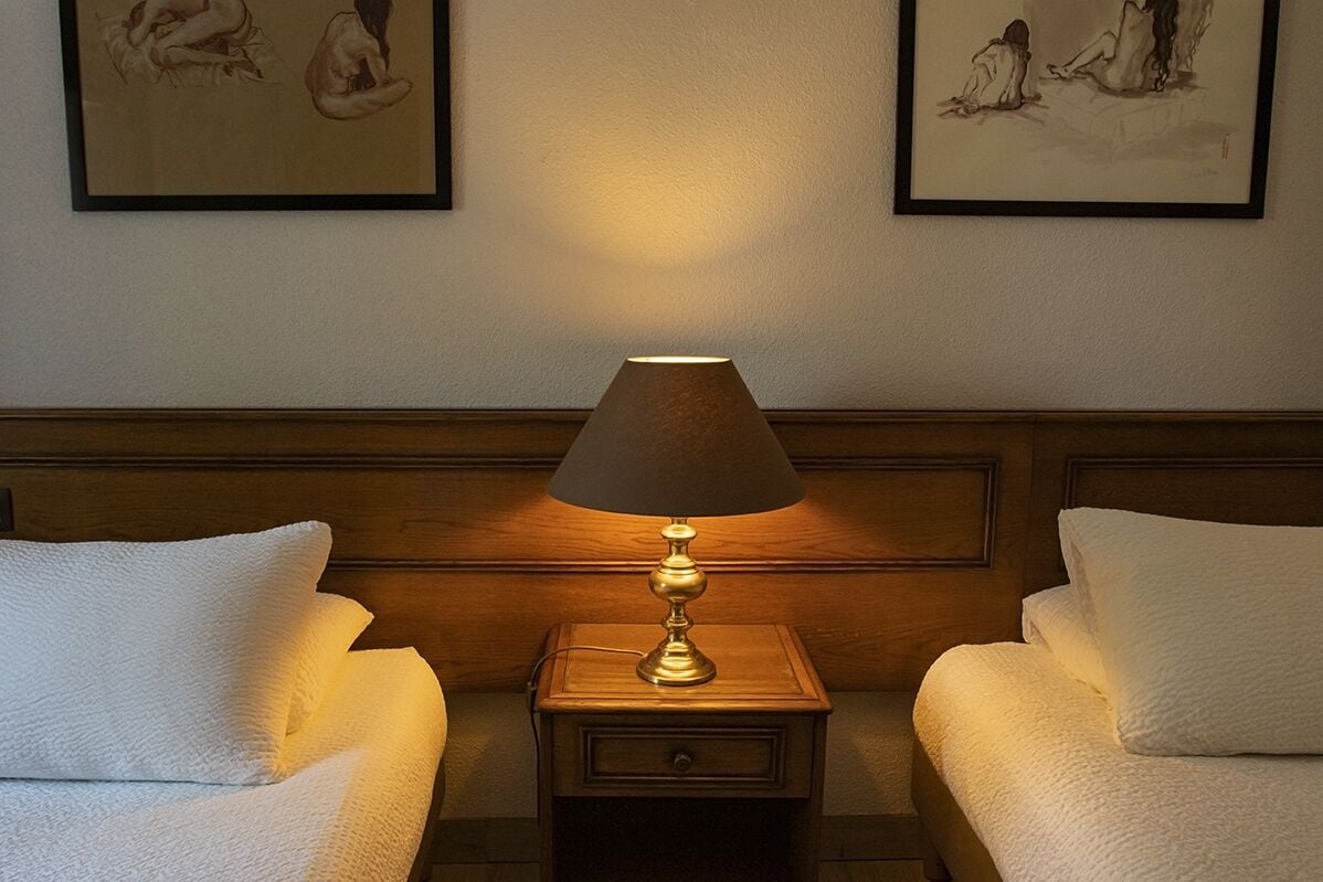 Une chambre d’hôtel avec deux lits, une table de chevet avec une lampe et des œuvres d’art encadrées accrochées au mur.