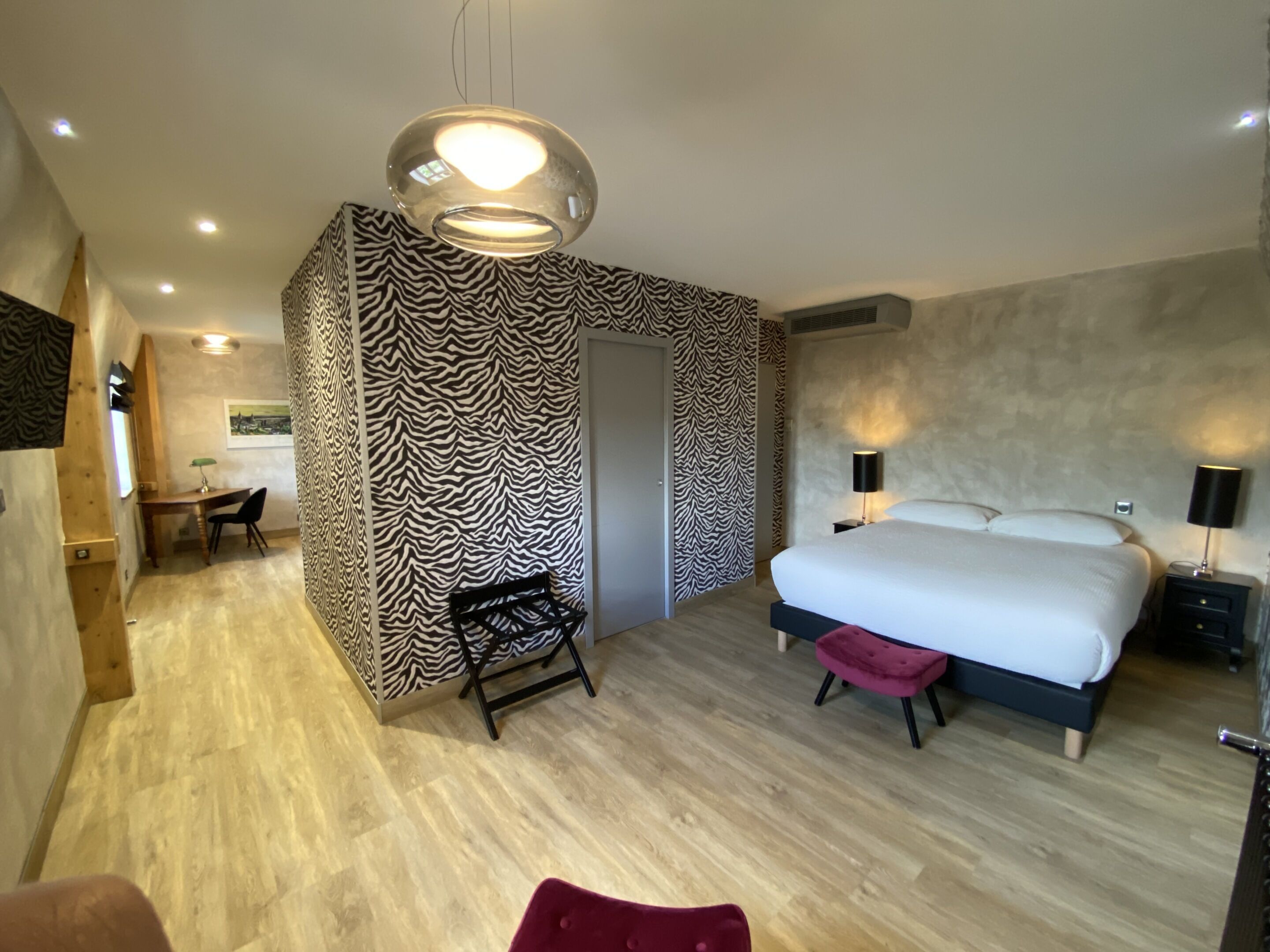 A modern bedroom with a zebra-patterned accent wall, a large bed with a red ottoman, and a desk with a chair.