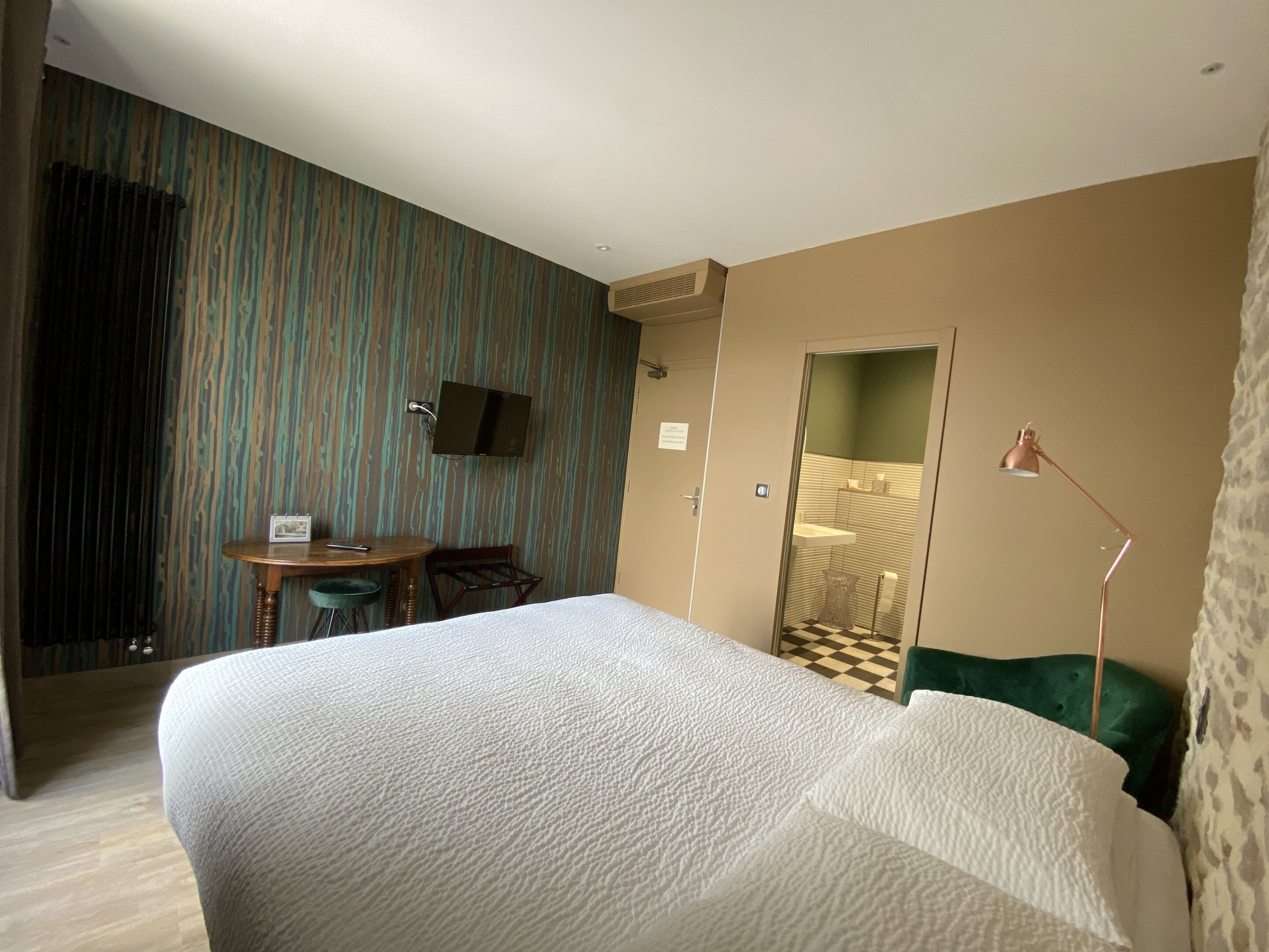 A hotel room with a large bed, a desk with a chair, a TV mounted on the wall, and a mirror.