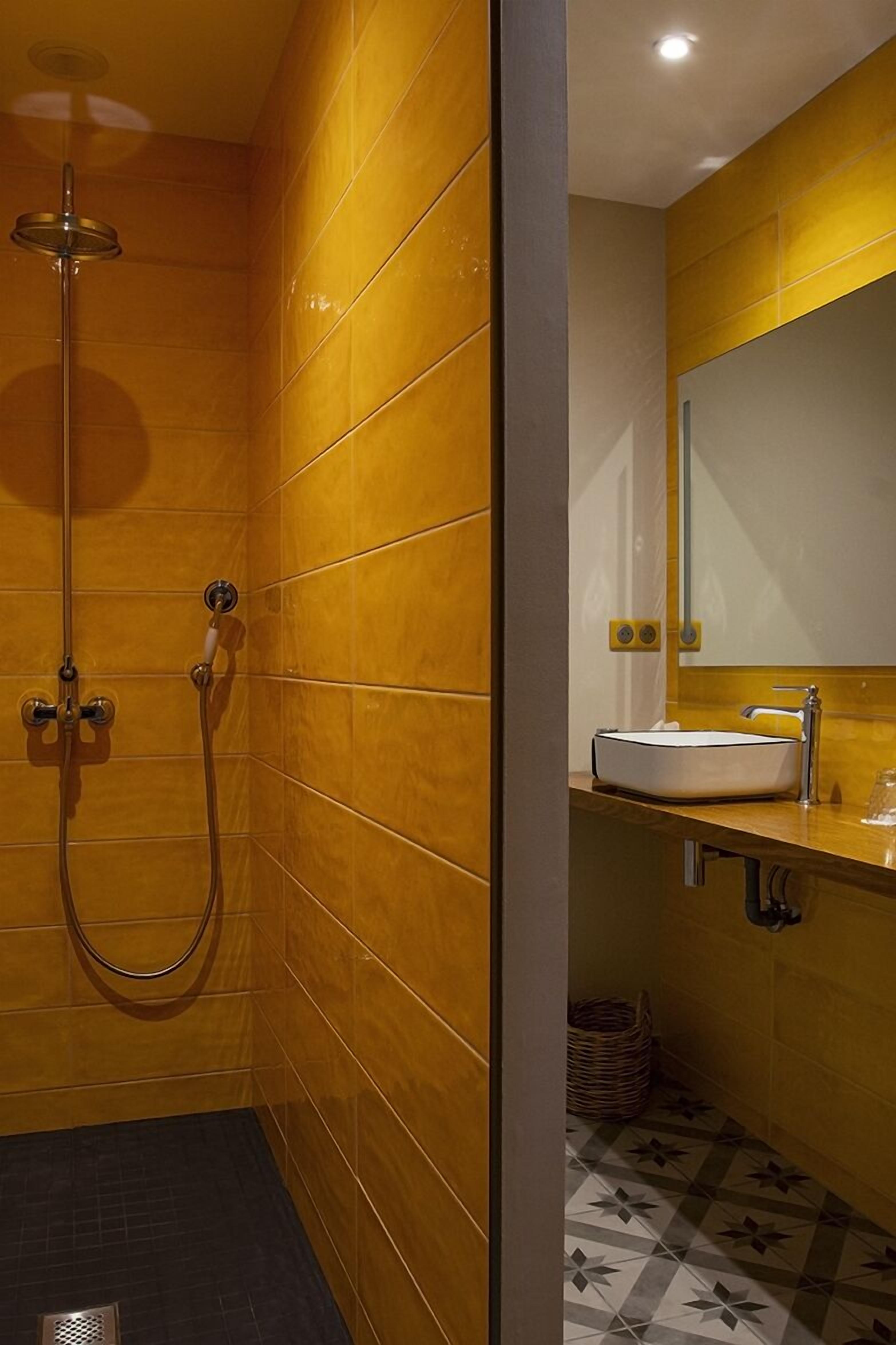 A modern bathroom with yellow tiled walls, a shower, a sink with a mirror, and patterned floor tiles.