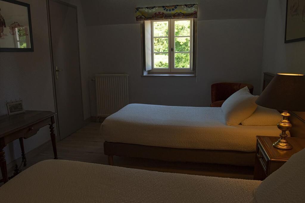 Un dormitorio con una cama individual, una mesita de noche con lámpara, una ventana con vistas a zonas verdes y un radiador.