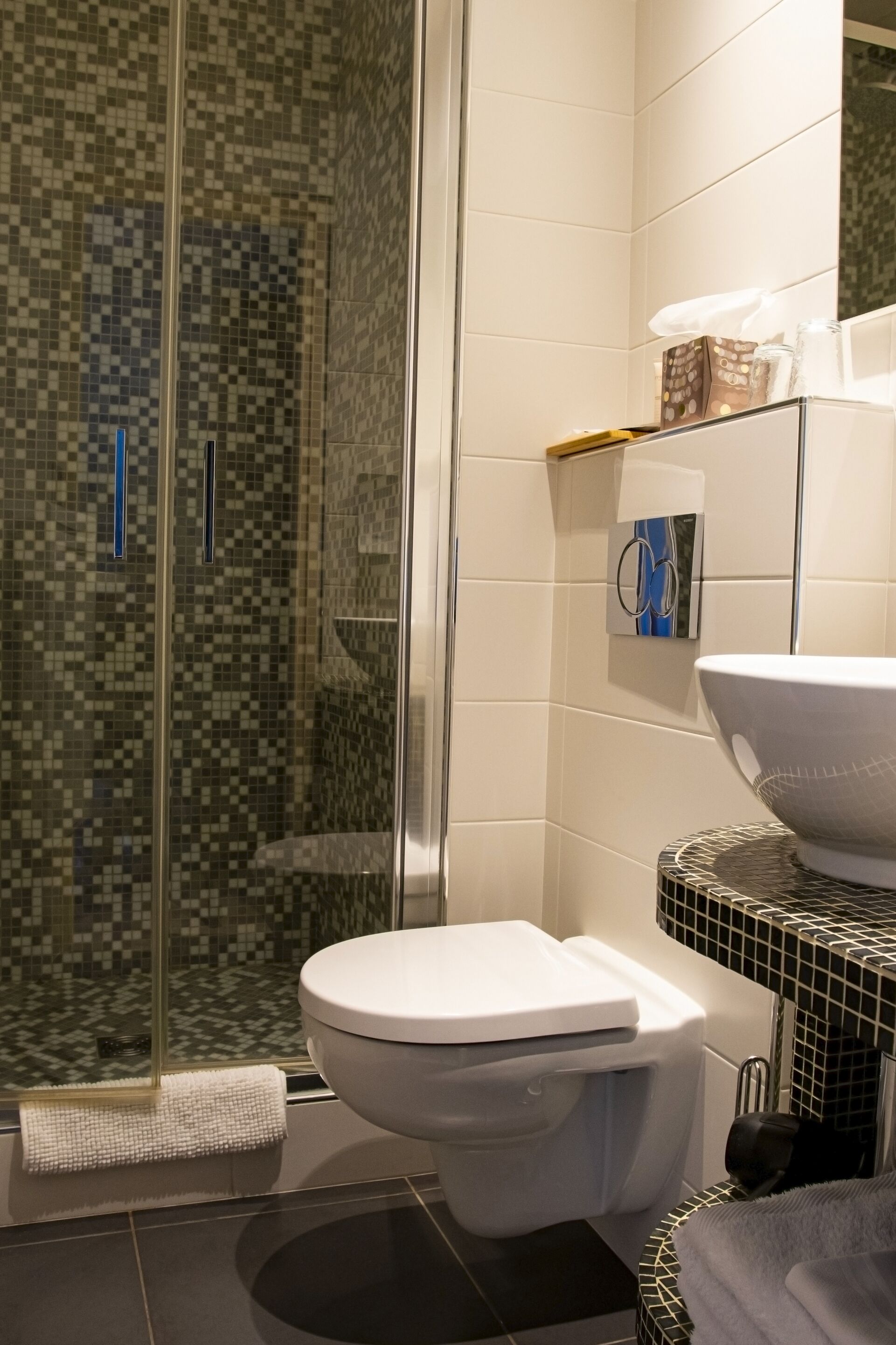 A modern bathroom with a glass-enclosed shower, a white toilet, and a sink with a mosaic tile backsplash.