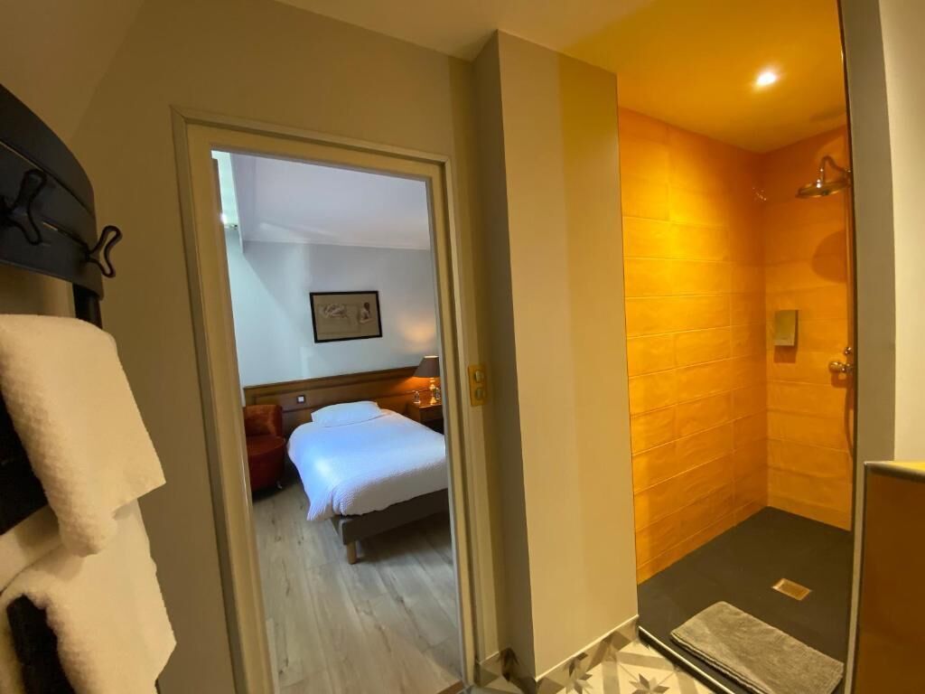 Una habitación de hotel con cama, una zona de estar pequeña y un área de ducha con pared de azulejos.