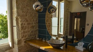 A bathroom with a stone wall, a wooden vanity, a large mirror, and a bowl sink. - Le Terminus (Tournus)