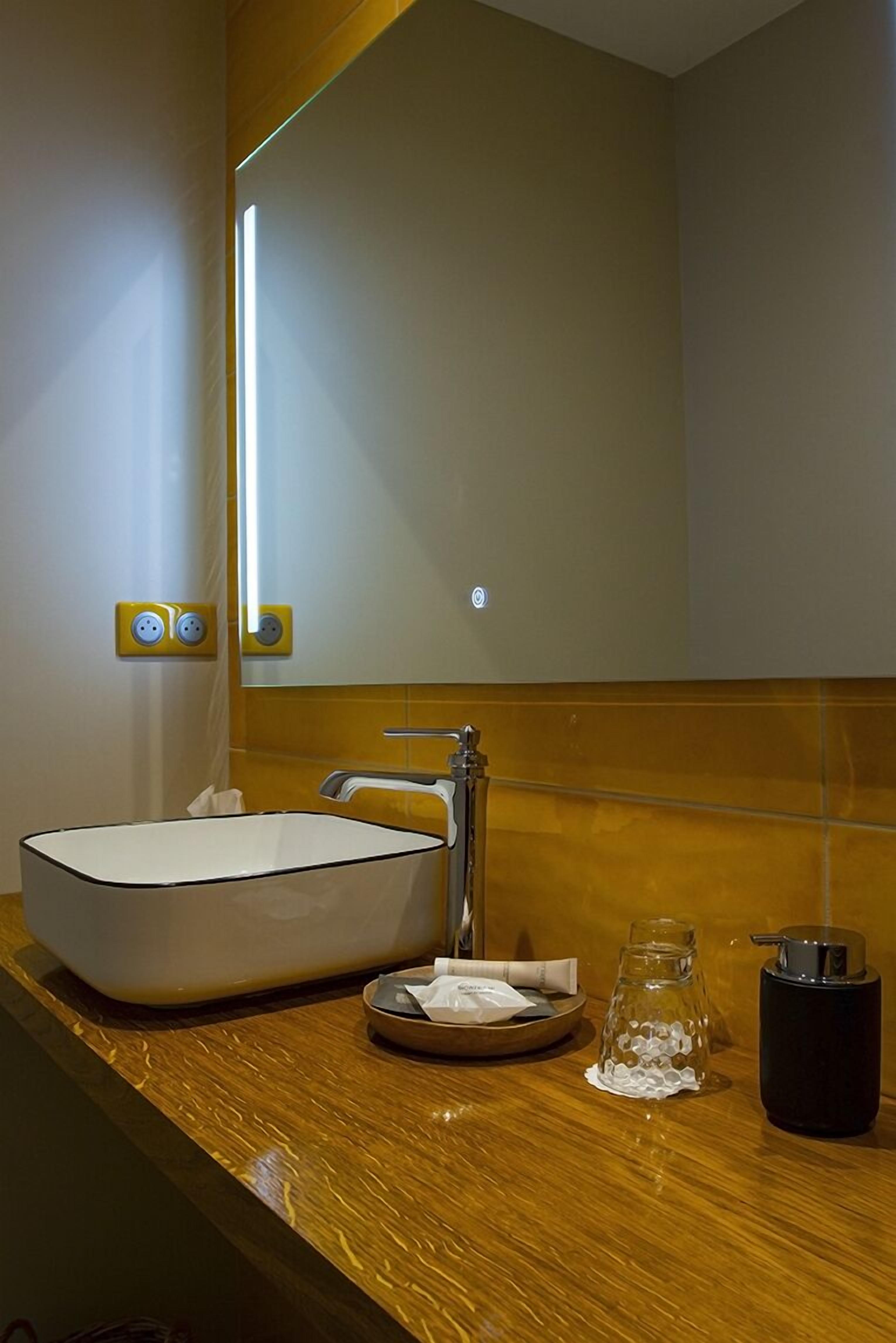 A bathroom with a large mirror, a vessel sink, a faucet, and a black container on the counter.