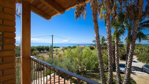 Un balcone con vista sul mare, palme e cielo azzurro.