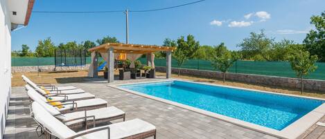 Una piscina con sillones de descanso y una pérgola.