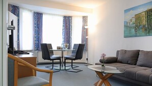 Et moderne hotelværelse med en træstol, et glasbord, en sofa og et bybillede.