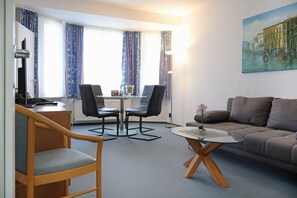 Et moderne hotelværelse med en træstol, et glasbord, en sofa og et bybillede.