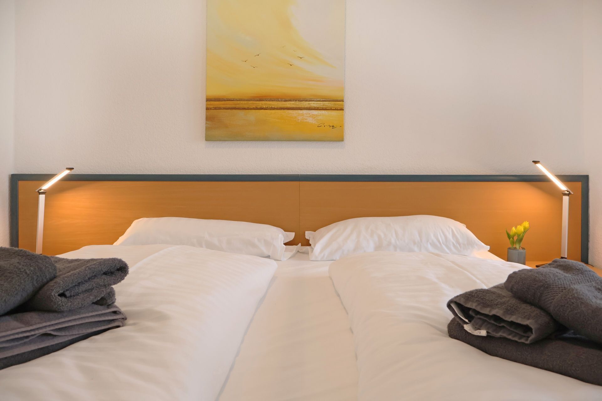 Et hotelværelse med en seng, puder og et billede på væggen.