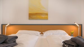 Et hotelværelse med en seng, puder og et billede på væggen.