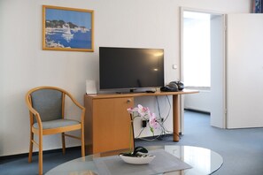 Et hotelværelse med skrivebord i træ, fjernsyn, stol og et lille bord med en orkidé i potte.